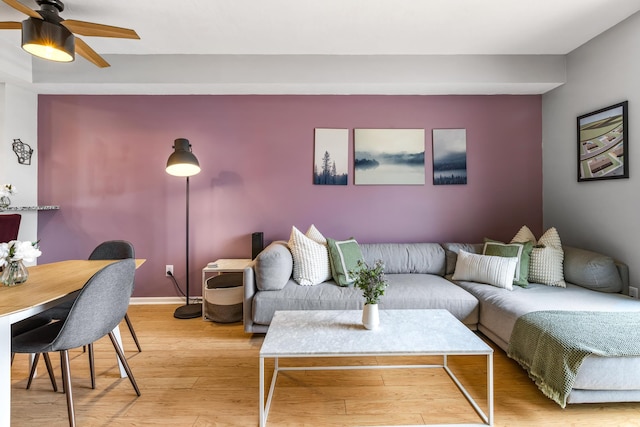 living area with light wood finished floors, a ceiling fan, and baseboards