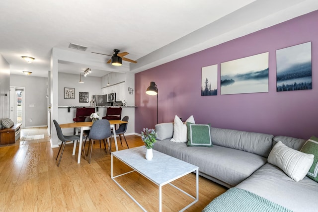 living area with light wood-style flooring, a ceiling fan, visible vents, and baseboards