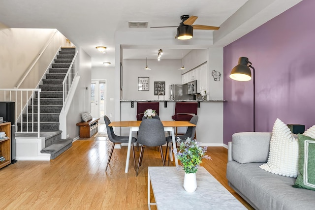 living room with visible vents, baseboards, ceiling fan, stairway, and light wood-style floors