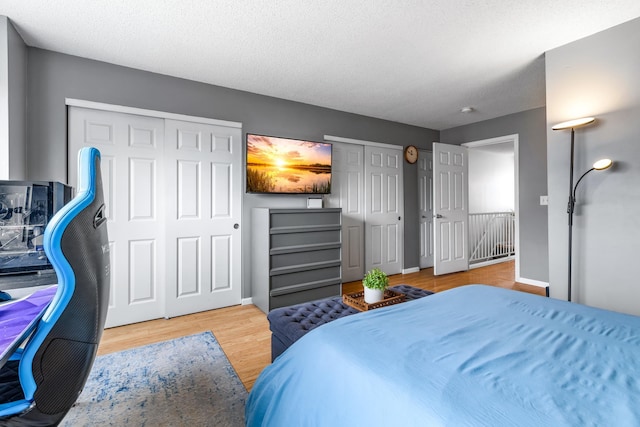 bedroom featuring baseboards, a textured ceiling, wood finished floors, and multiple closets