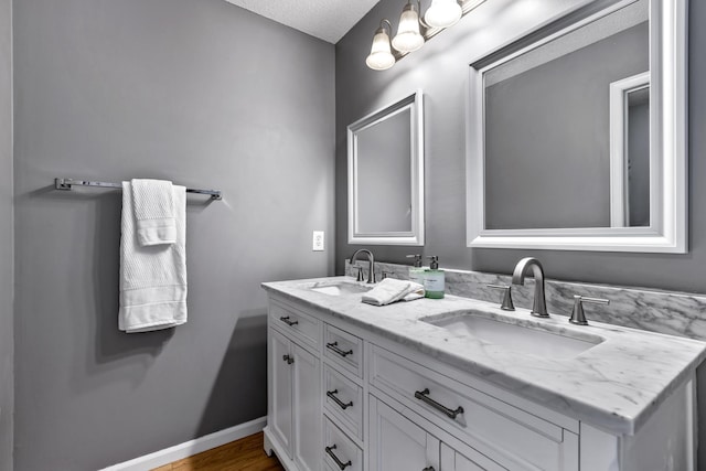 full bathroom featuring double vanity, wood finished floors, a sink, and baseboards