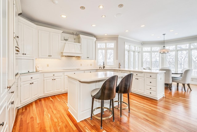 kitchen with light countertops, custom exhaust hood, a kitchen island, and white cabinets