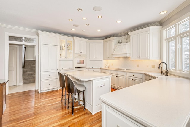 kitchen featuring light countertops, custom range hood, glass insert cabinets, a kitchen island, and black electric cooktop