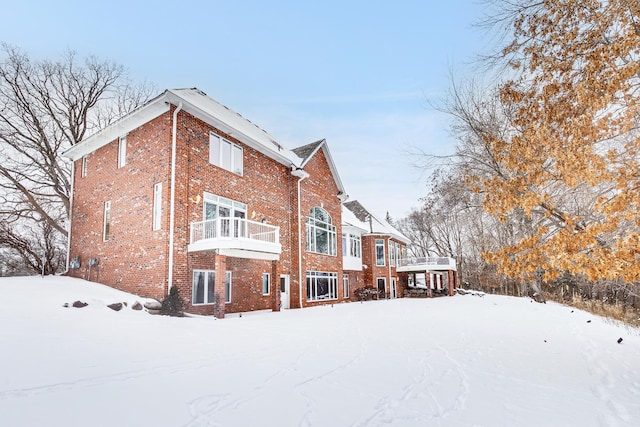 snow covered back of property with brick siding and a balcony