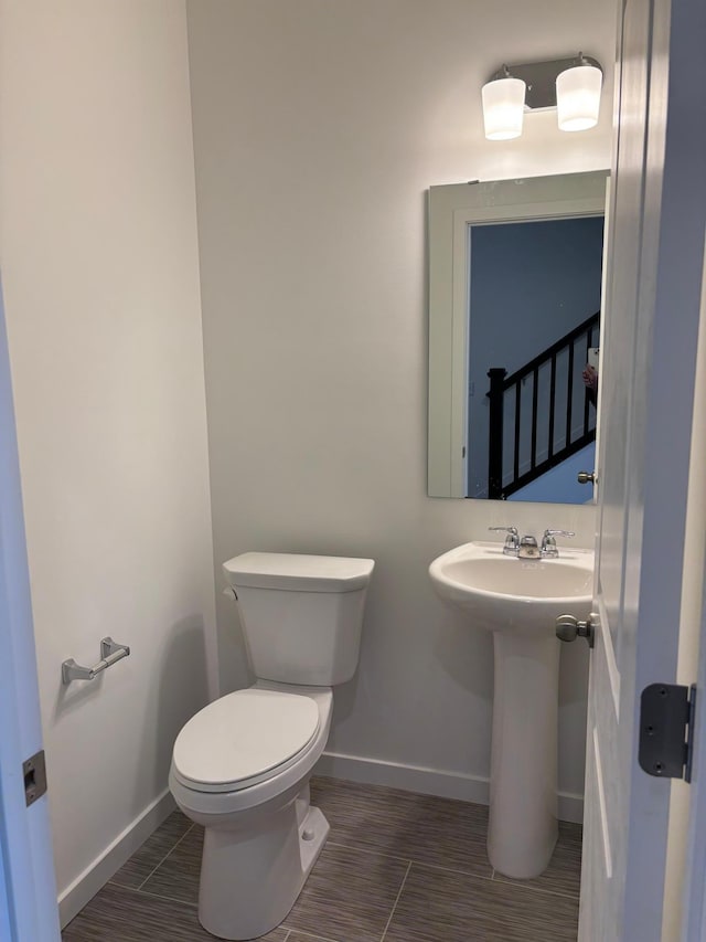 half bath with toilet, baseboards, and a sink