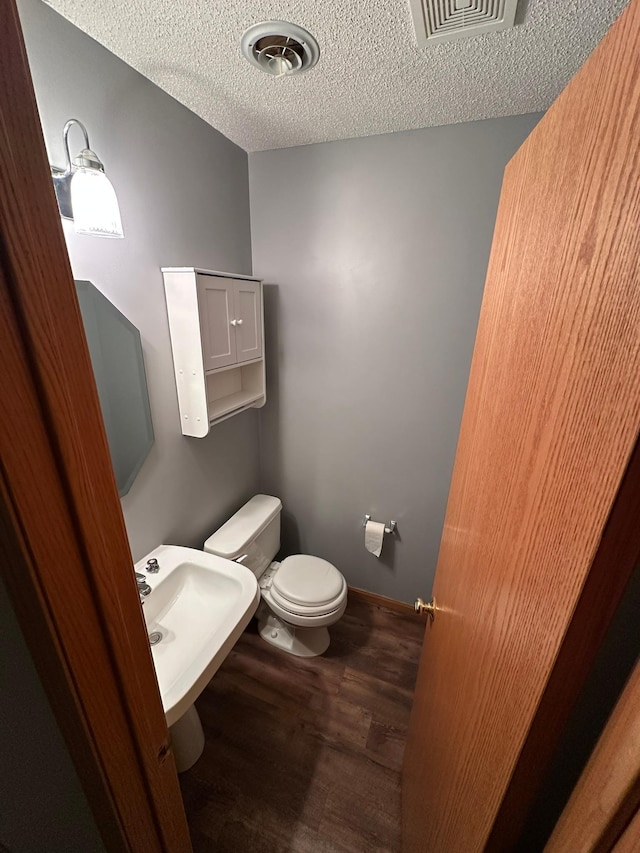 half bath featuring toilet, wood finished floors, visible vents, and a textured ceiling