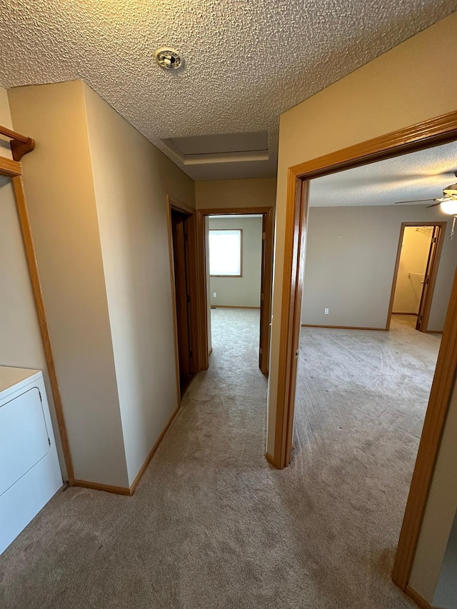 hall with washer / dryer, carpet flooring, baseboards, and a textured ceiling