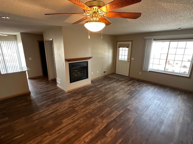 unfurnished living room with dark wood-style floors, baseboards, ceiling fan, a textured ceiling, and a glass covered fireplace