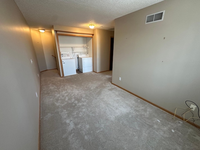 interior space with visible vents, independent washer and dryer, a textured ceiling, baseboards, and light colored carpet