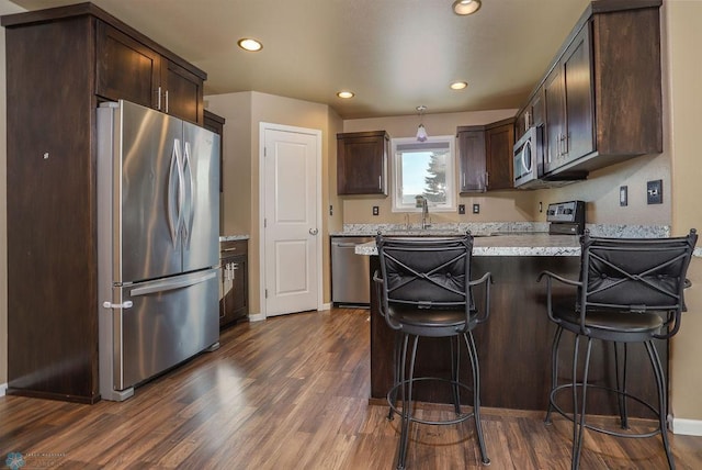 kitchen featuring dark brown cabinets, appliances with stainless steel finishes, dark wood finished floors, and a kitchen breakfast bar