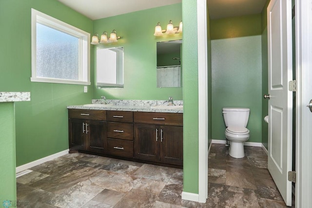 full bathroom with baseboards, a sink, toilet, and double vanity