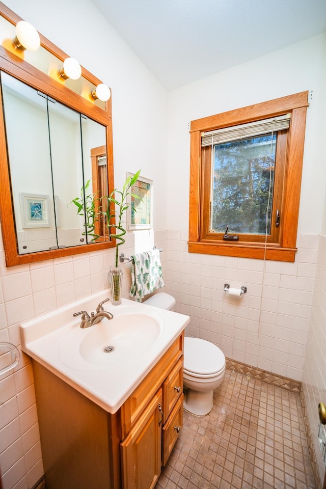 bathroom with toilet, a wainscoted wall, tile walls, and vanity