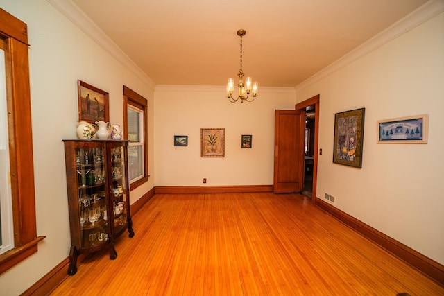 unfurnished room featuring crown molding, a notable chandelier, visible vents, wood finished floors, and baseboards