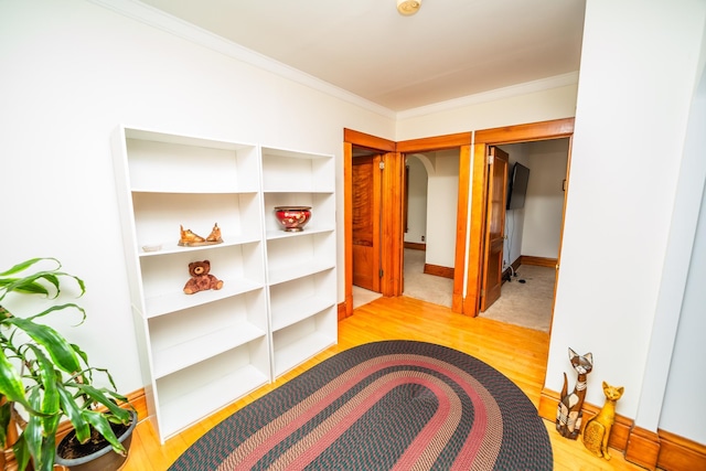 hallway featuring light wood-style floors, arched walkways, crown molding, and baseboards