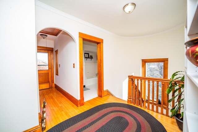 hall with arched walkways, ornamental molding, an upstairs landing, wood finished floors, and baseboards