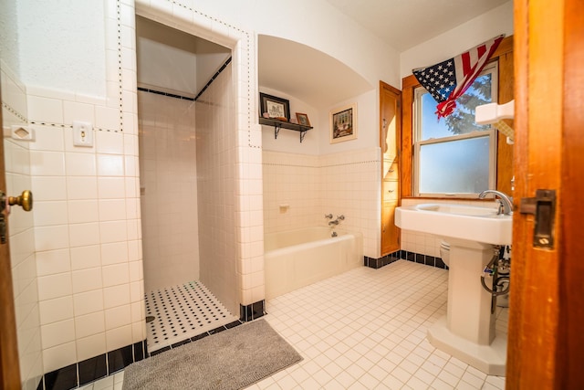 bathroom featuring a wainscoted wall, tile patterned flooring, tile walls, and a bath