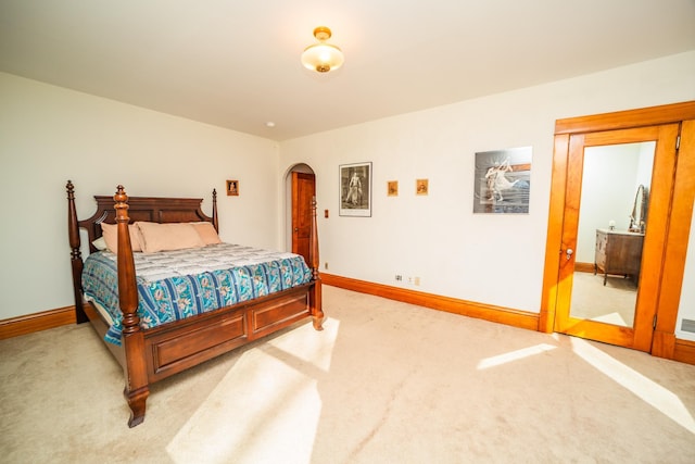 bedroom featuring arched walkways, light colored carpet, and baseboards