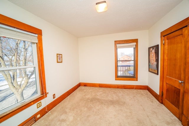 spare room with light carpet, baseboards, and a textured ceiling