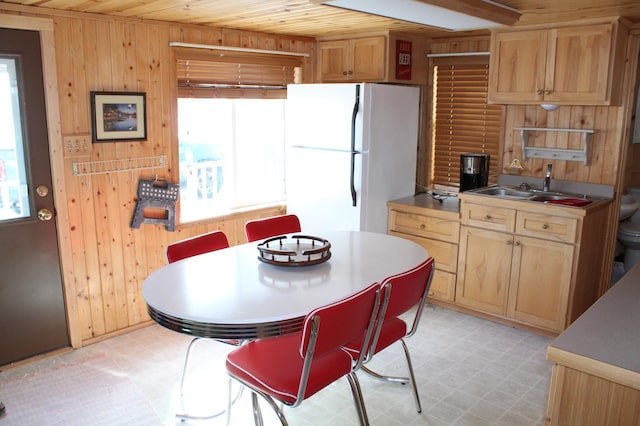 kitchen featuring light floors, wooden walls, a sink, and freestanding refrigerator