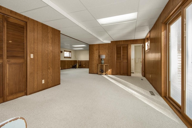 carpeted spare room featuring a paneled ceiling, wooden walls, and visible vents