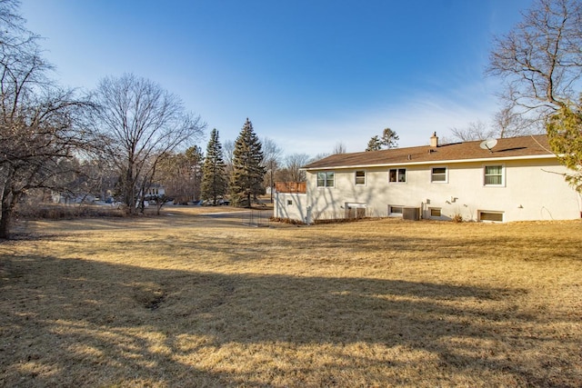 rear view of house with a yard, a chimney, and stucco siding