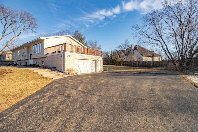 view of property exterior featuring a garage, brick siding, driveway, and fence