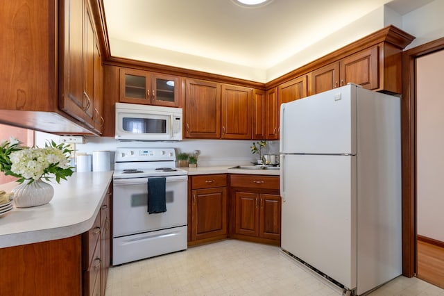 kitchen with brown cabinets, white appliances, light countertops, glass insert cabinets, and light floors