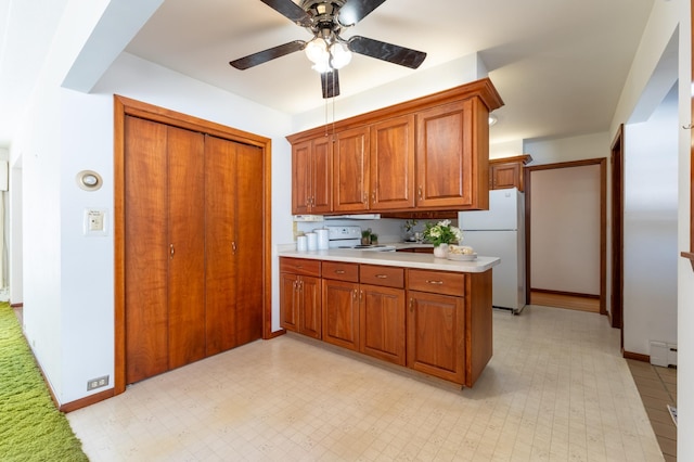 kitchen featuring white appliances, a peninsula, brown cabinetry, light countertops, and light floors