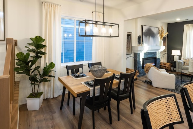 dining area featuring an inviting chandelier, plenty of natural light, wood finished floors, and a glass covered fireplace