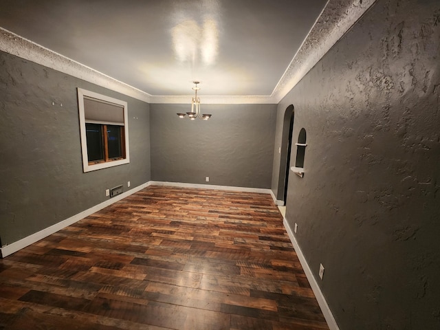 unfurnished room featuring a textured wall, ornamental molding, dark wood finished floors, and an inviting chandelier