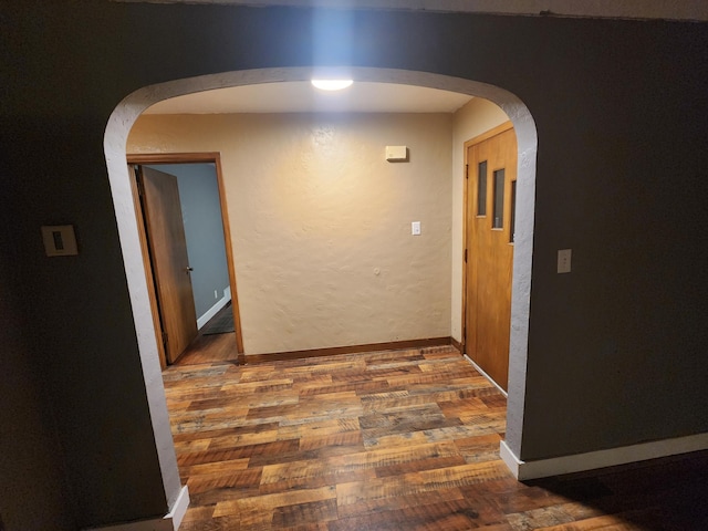 corridor with dark wood-style floors, arched walkways, and baseboards