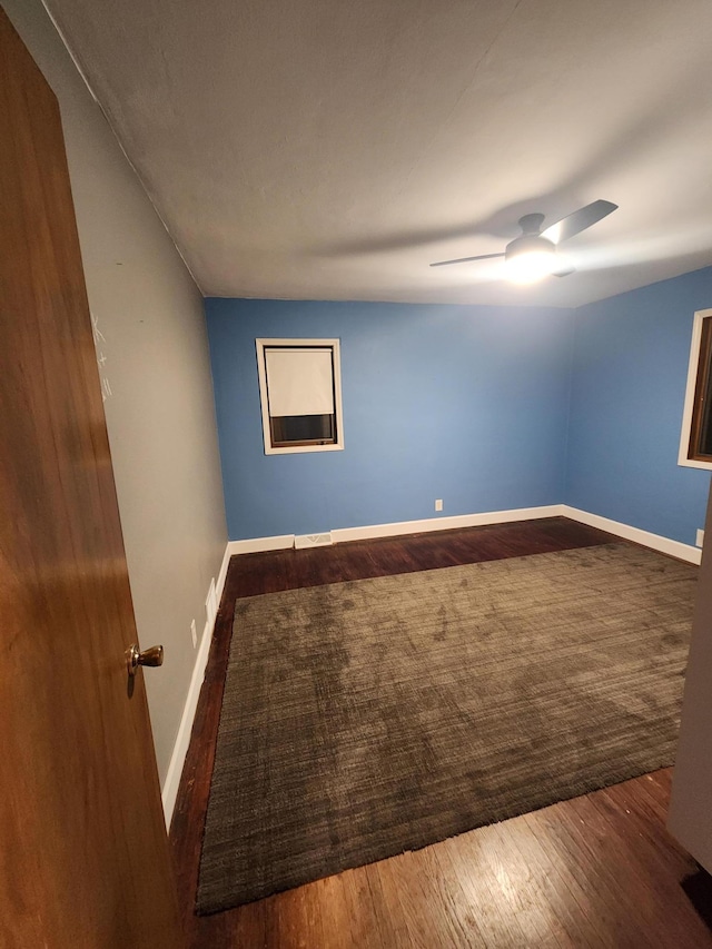 empty room with dark wood-style floors, visible vents, ceiling fan, and baseboards