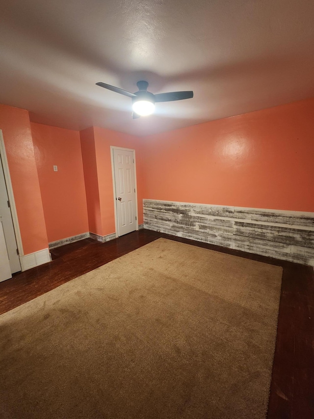 empty room with a ceiling fan, dark carpet, and baseboards