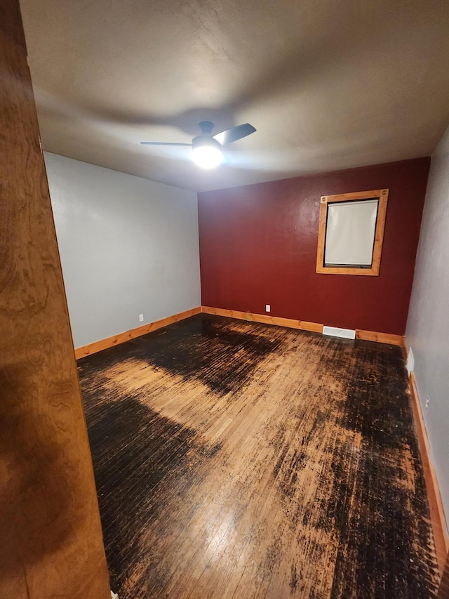 spare room with a ceiling fan, visible vents, baseboards, and wood finished floors