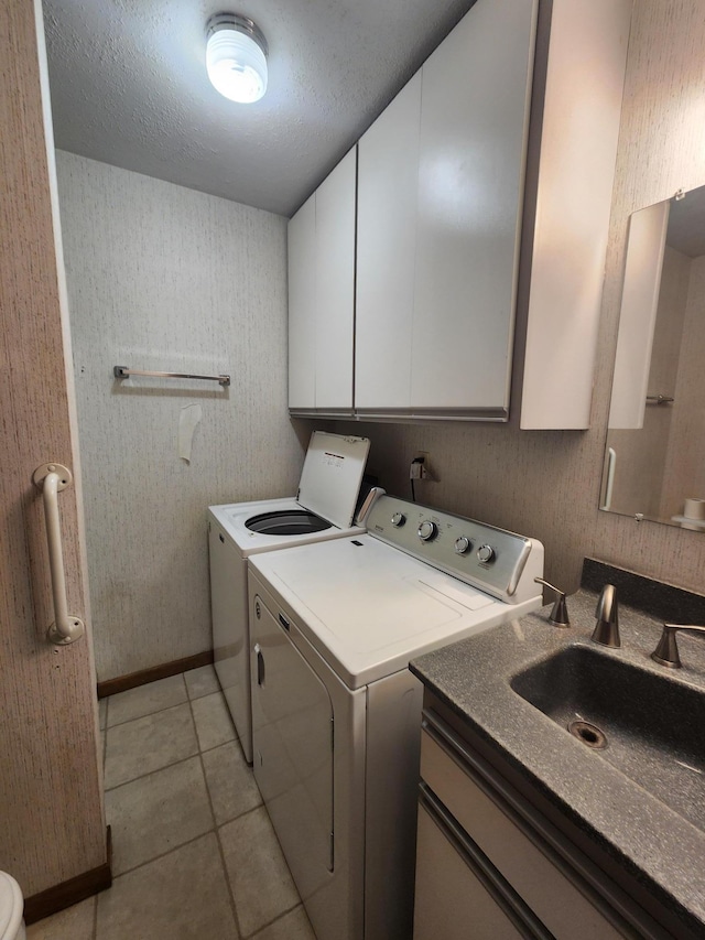 clothes washing area featuring light tile patterned floors, a textured ceiling, separate washer and dryer, a sink, and cabinet space