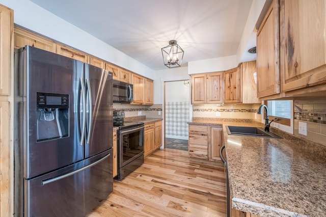 kitchen with hanging light fixtures, a sink, stainless steel appliances, light wood-style floors, and backsplash