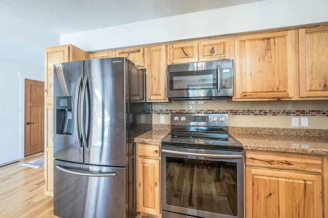 kitchen with tasteful backsplash, appliances with stainless steel finishes, light wood-type flooring, and light stone countertops