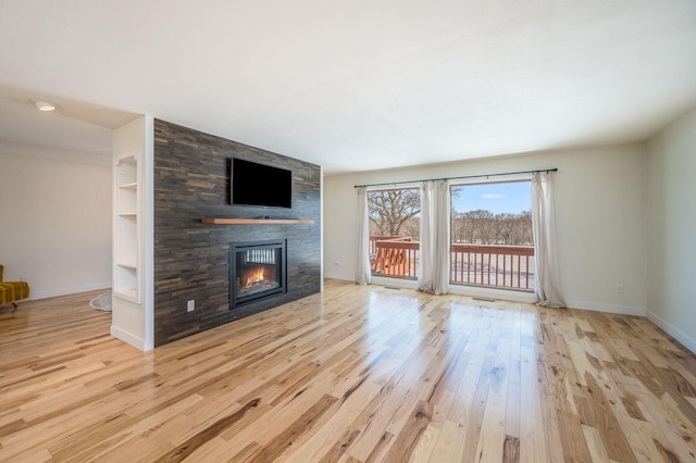 unfurnished living room featuring light wood-style floors, baseboards, built in features, and a stone fireplace