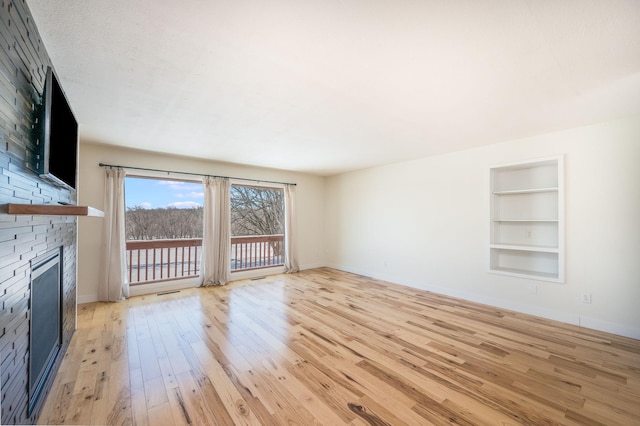 unfurnished living room featuring built in shelves, baseboards, and light wood finished floors