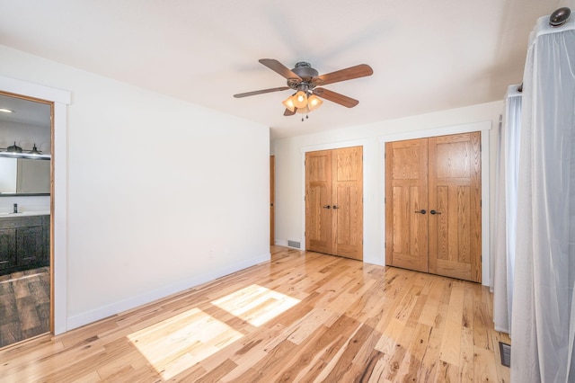 unfurnished bedroom featuring light wood finished floors, multiple closets, visible vents, ceiling fan, and baseboards