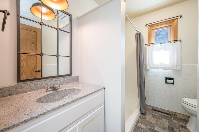 full bath with tile walls, visible vents, a shower with shower curtain, stone finish flooring, and vanity