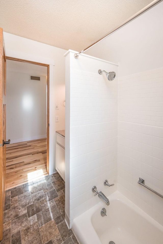 full bathroom with bathing tub / shower combination, visible vents, stone finish floor, vanity, and a textured ceiling