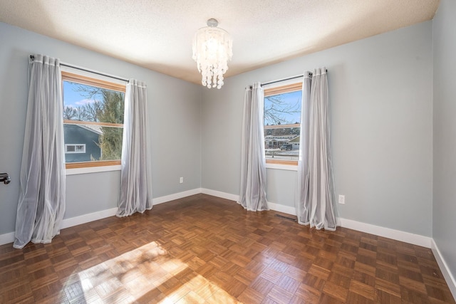 empty room featuring a healthy amount of sunlight, a notable chandelier, a textured ceiling, and baseboards