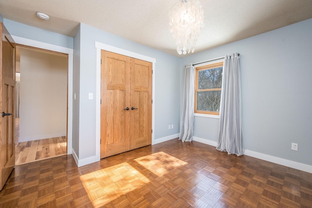 unfurnished bedroom featuring a textured ceiling, a closet, baseboards, and a notable chandelier