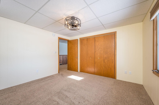 unfurnished bedroom with carpet floors, a paneled ceiling, a closet, and an inviting chandelier