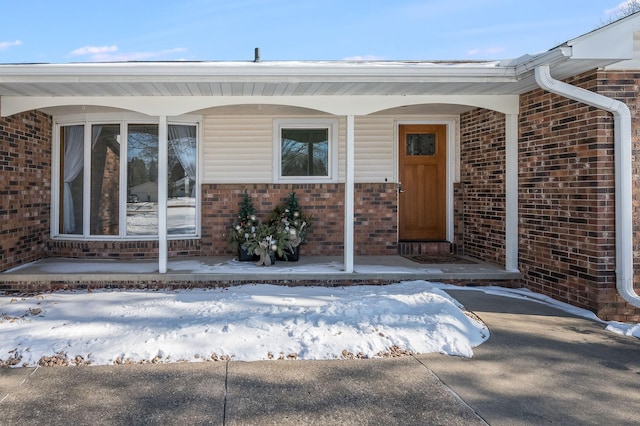 snow covered property entrance with brick siding