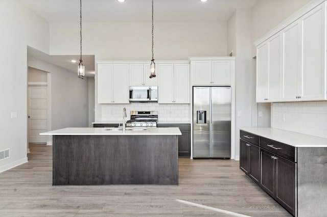 kitchen with stainless steel appliances, light countertops, a center island with sink, and white cabinetry