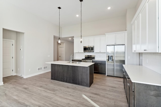 kitchen with a kitchen island with sink, white cabinetry, light countertops, appliances with stainless steel finishes, and decorative light fixtures