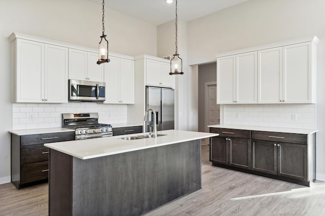 kitchen with appliances with stainless steel finishes, hanging light fixtures, a kitchen island with sink, light countertops, and a sink