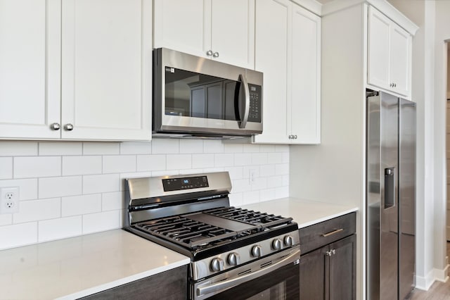 kitchen with white cabinets, appliances with stainless steel finishes, light countertops, dark brown cabinets, and backsplash